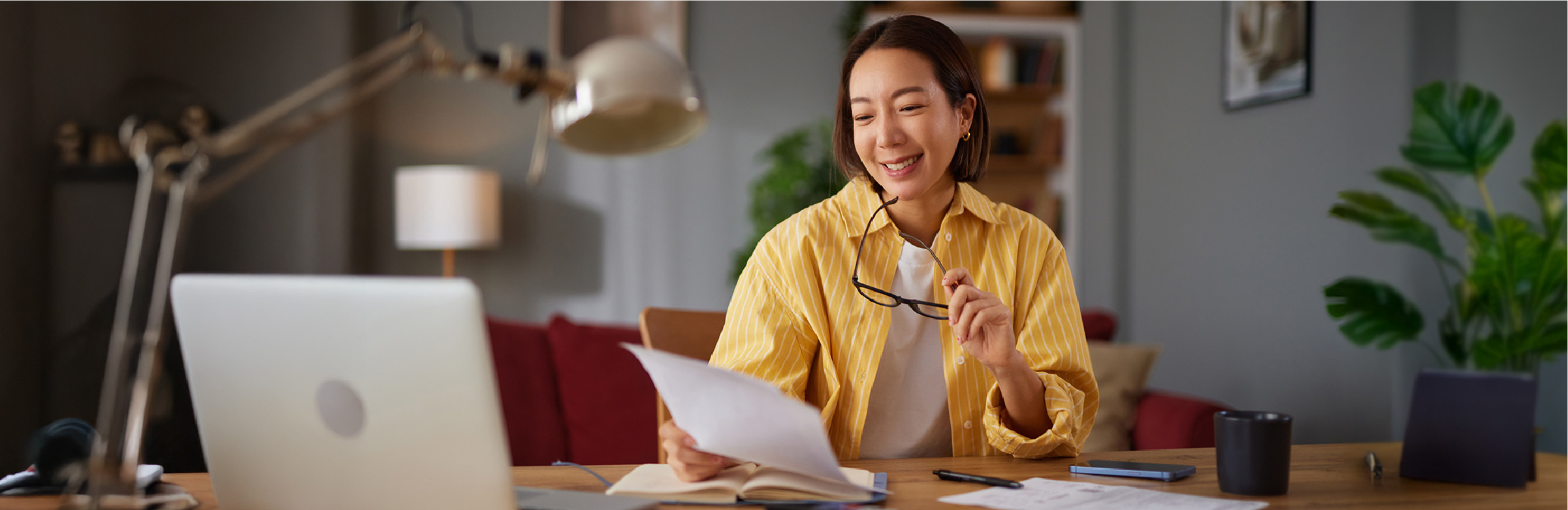 Femme examinant des documents financiers à son bureau à domicile avec ordinateur portable