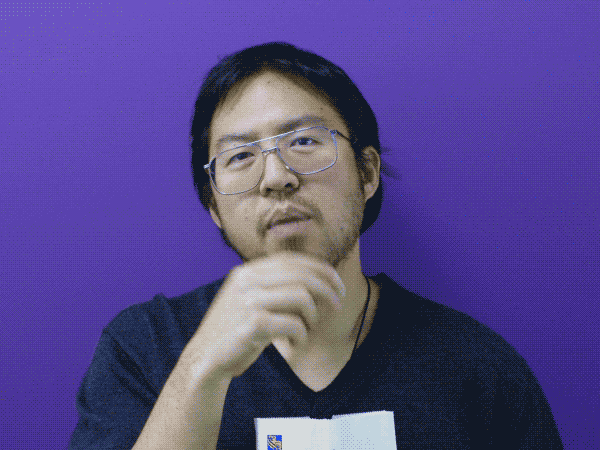 Un homme asiatique portant des lunettes et semblant s’ennuyer mange du maïs soufflé.