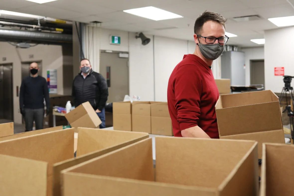 Three masked volunteers sort food donations into boxes inside the Regina Food Bank.