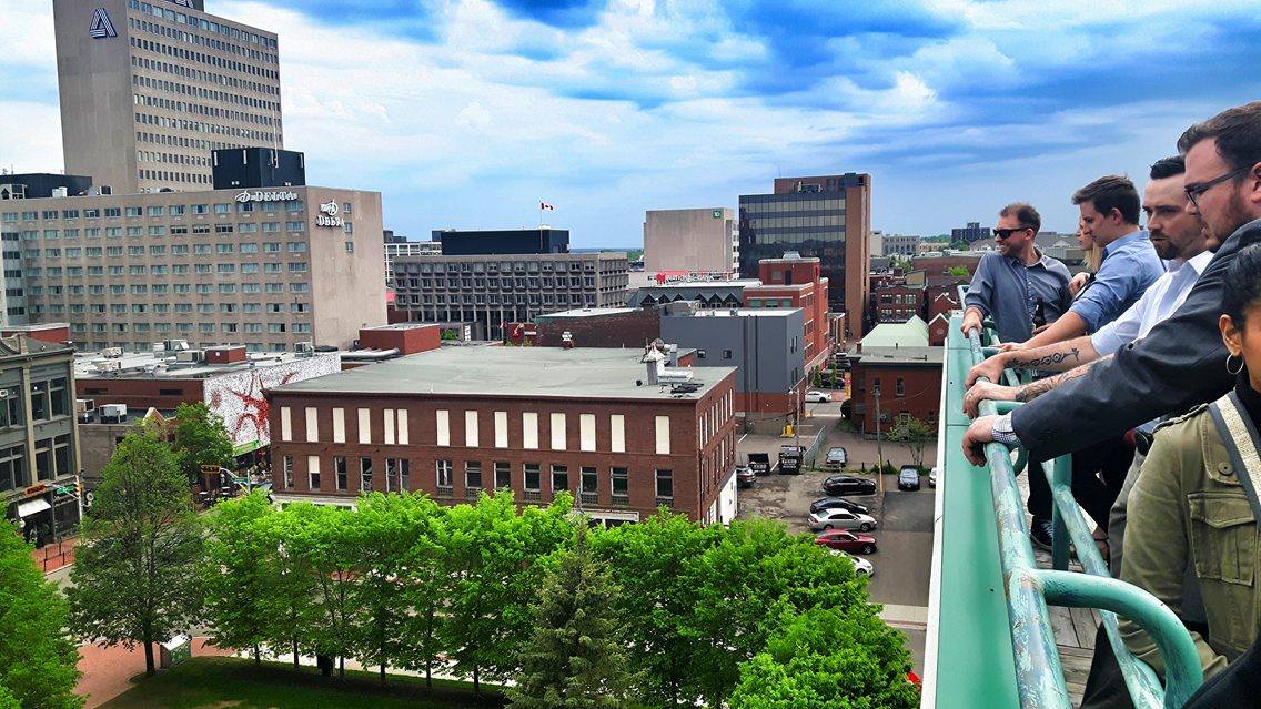 Groupe de jeunes professionnels sur un balcon donnant sur le centre-ville de Moncton.