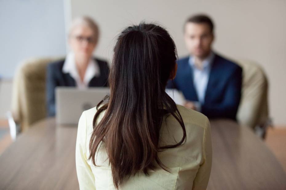 Une candidate assise dos à la caméra est interviewée par deux professeurs d'université.