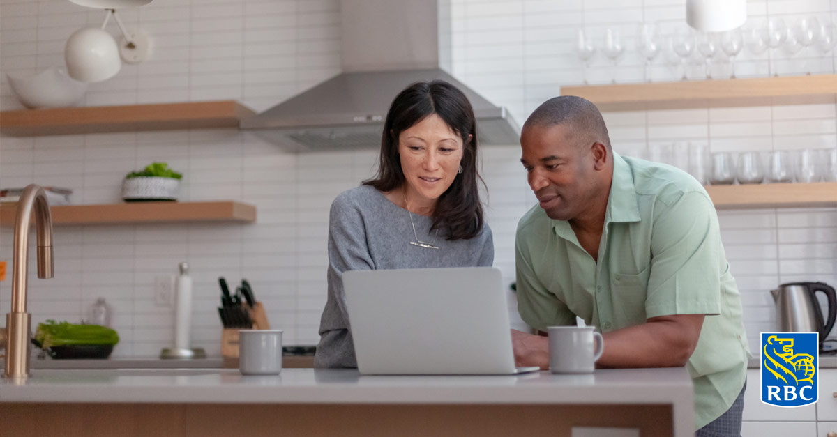 Image d'un couple heureux d'un certain âge qui regarde l'écran d'un portable placé sur le comptoir de cuisine.