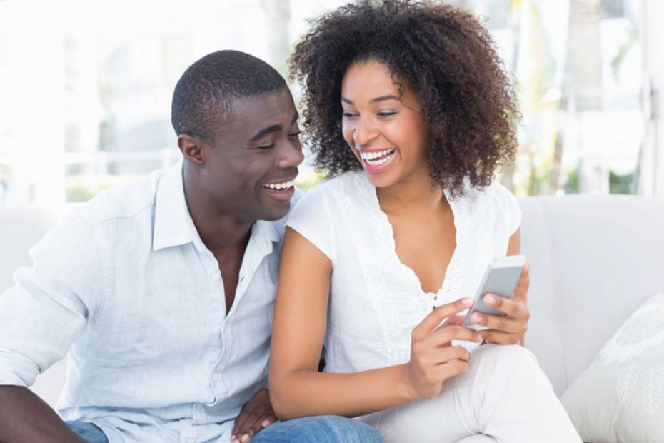 Image d'un couple assis sur un sofa, qui regarde en riant l'écran du téléphone que tient la femme.