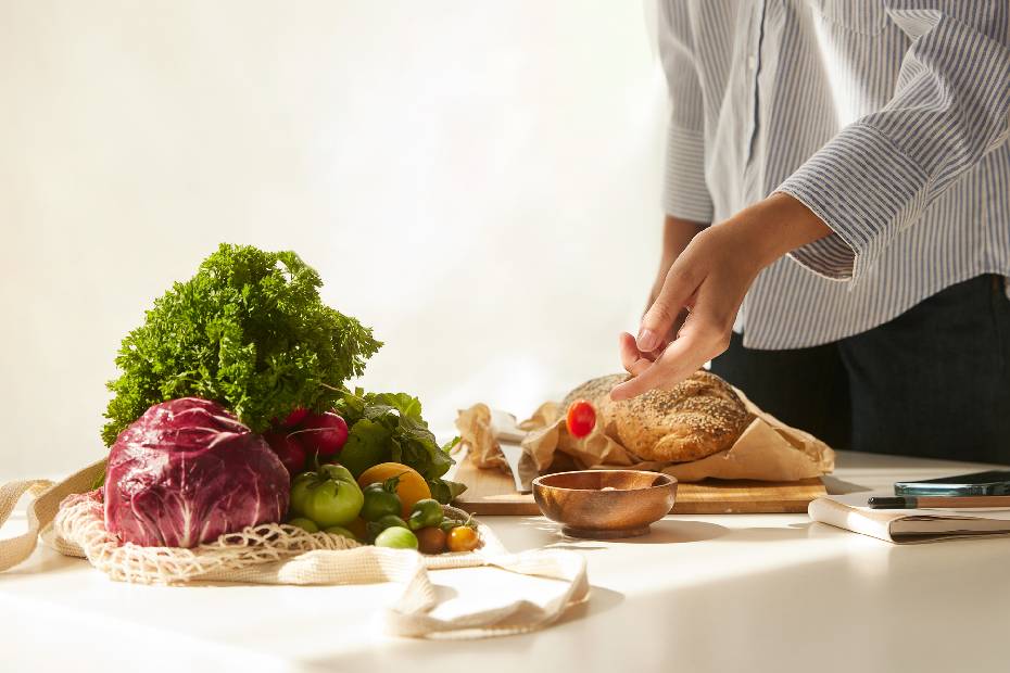 Une main dépose une tomate cerise dans un bol placé sur une table avec des légumes et du pain