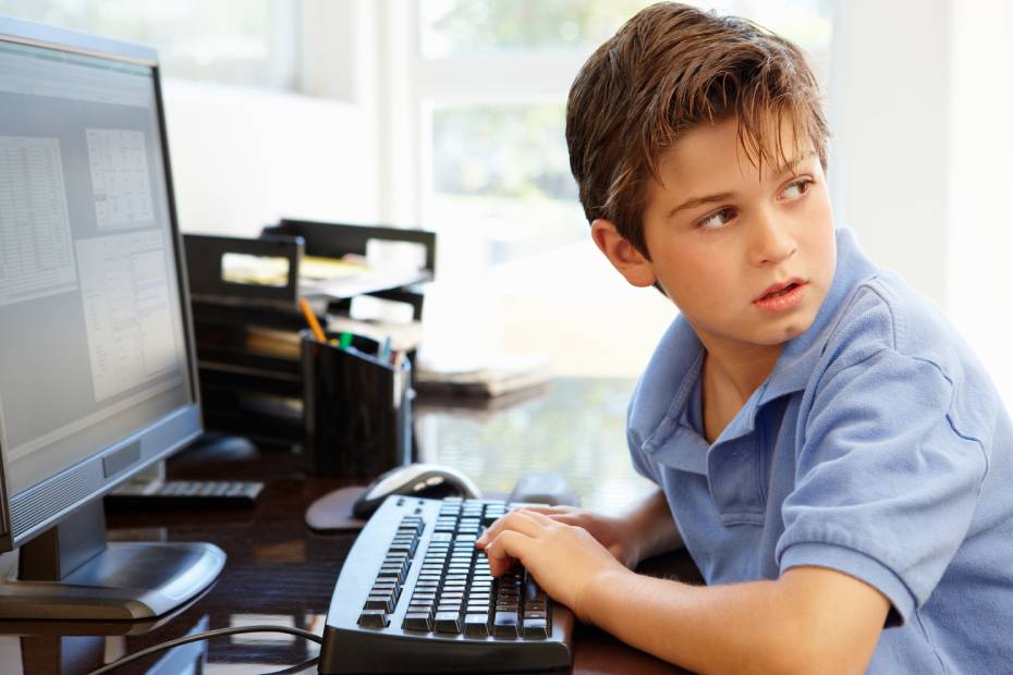 Jeune garçon tapant sur un ordinateur, regardant par-dessus son épaule.