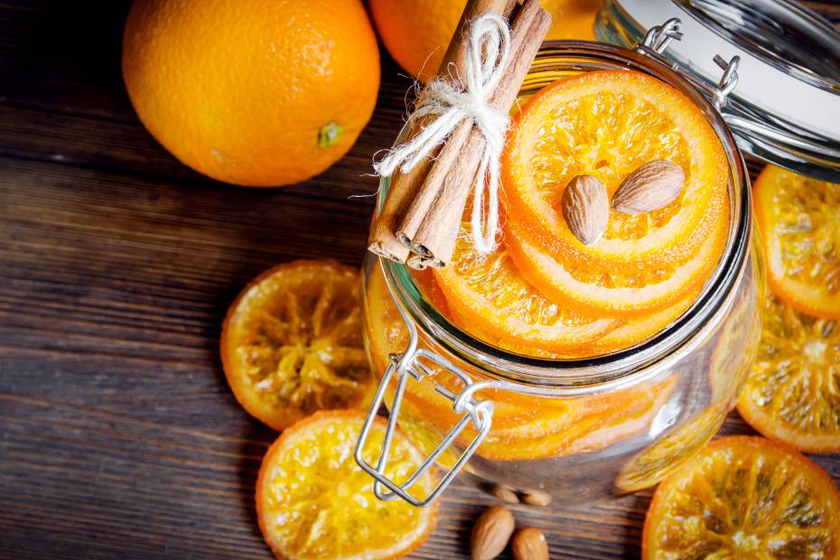 Oranges confites dans un bocal en verre avec bâtonnets de cannelle et amandes.