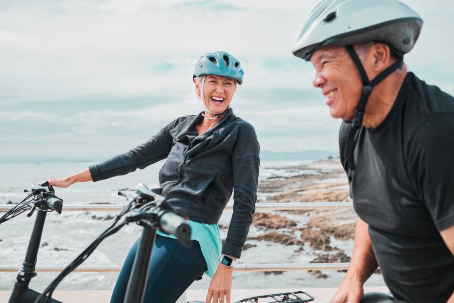 Couple âgé riant sur des vélos électriques près d’un lac