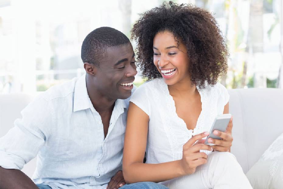 Image d'un couple assis sur un sofa, qui regarde en riant l'écran du téléphone que tient la femme.