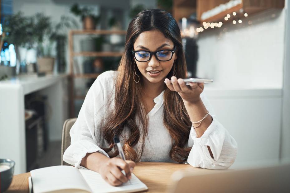 Une jeune femme parle au téléphone en prenant des notes.