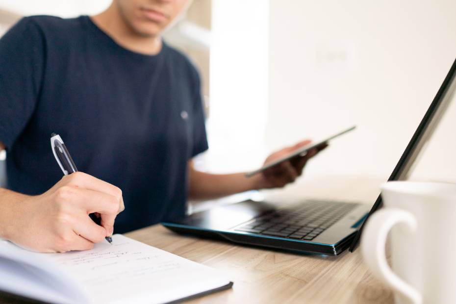 Gros plan d'un jeune homme qui prend des notes en consultant son ordinateur portatif