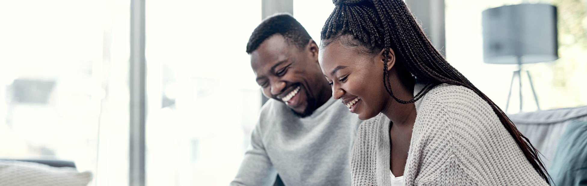 Un couple noir souriant assis sur un canapé blanc, examinant les options de paiement hypothécaire sur une tablette
