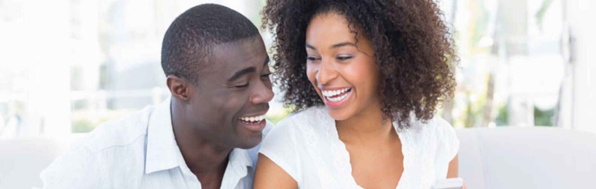 Image d'un couple assis sur un sofa, qui regarde en riant l'écran du téléphone que tient la femme.