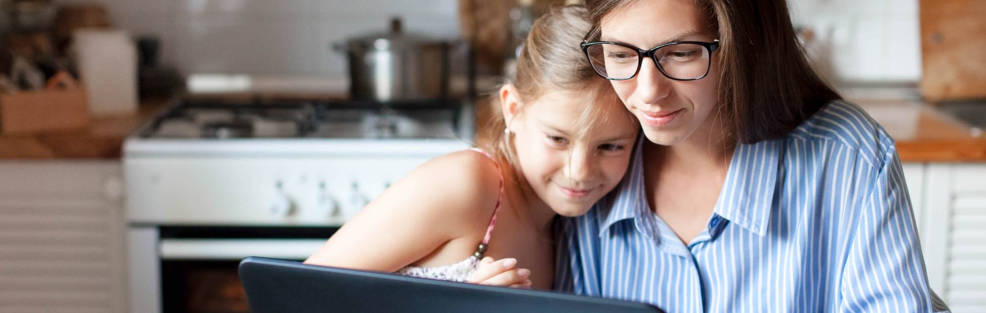 Une mère et sa fille souriantes s'embrassant, regardant un ordinateur portable