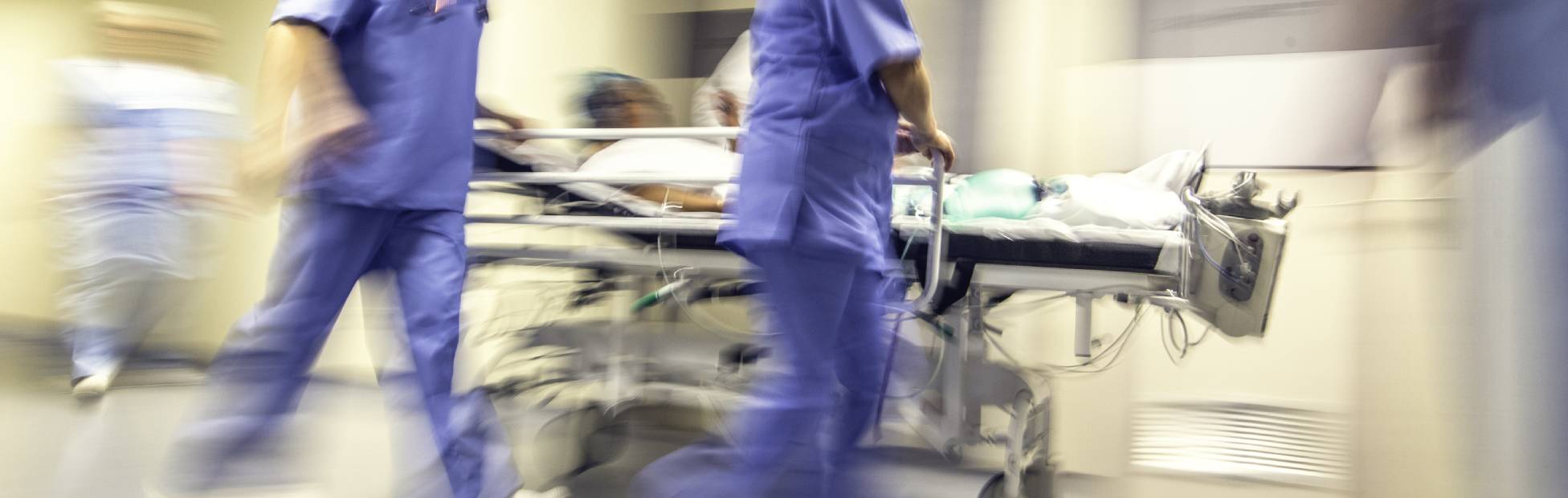 Image floue d'un médecin et d'un infirmier déplaçant rapidement une civière le long d'un couloir d'hôpital.