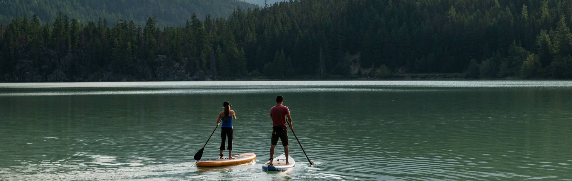 Deux personnes naviguent en planche à pagaie sur un lac entouré de paysages de montagne.