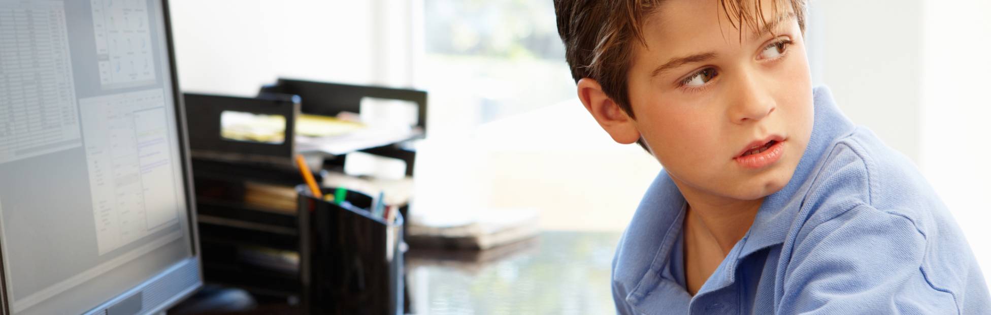 Jeune garçon tapant sur un ordinateur, regardant par-dessus son épaule.