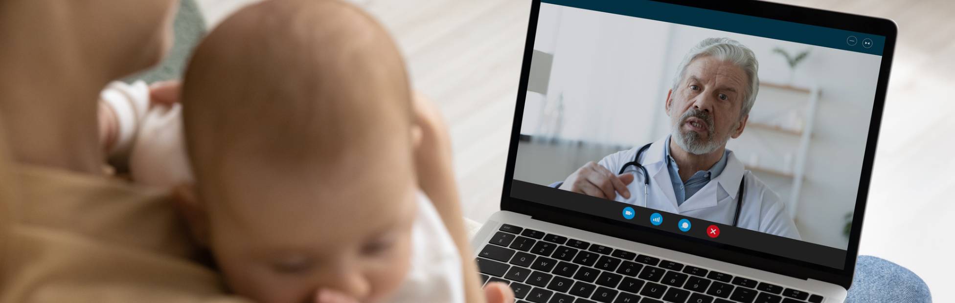 L'image montre une mère tenant son bébé et utilisant un ordinateur portable pour faire un appel vidéo avec un pédiatre.