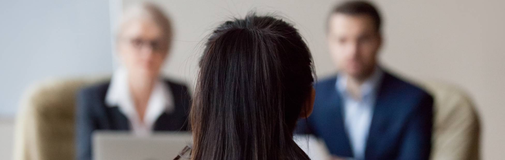 Une candidate assise dos à la caméra est interviewée par deux professeurs d'université.