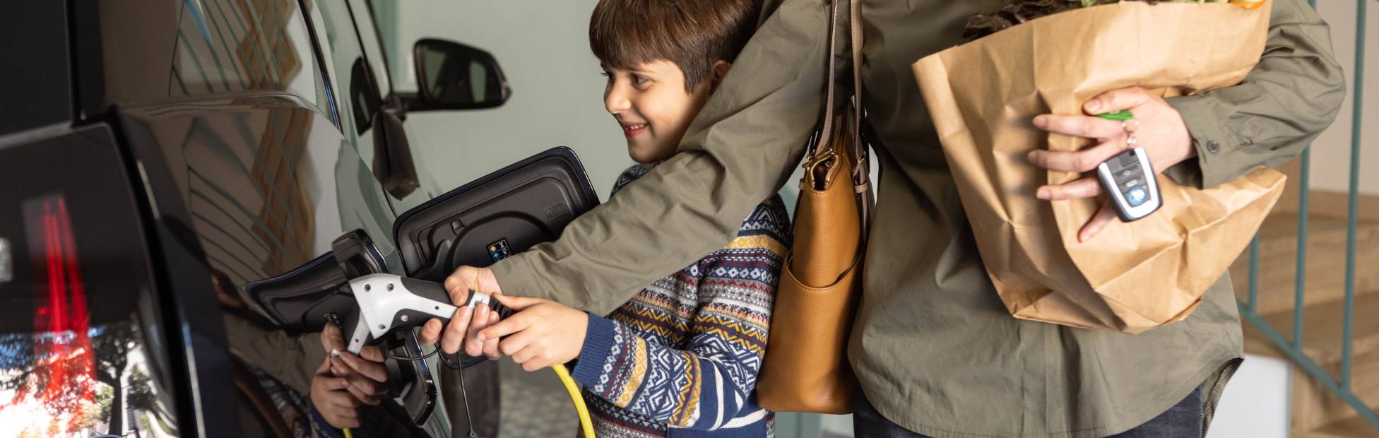 Un parent en compagnie d'un enfant recharge son véhicule électrique à domicile.
