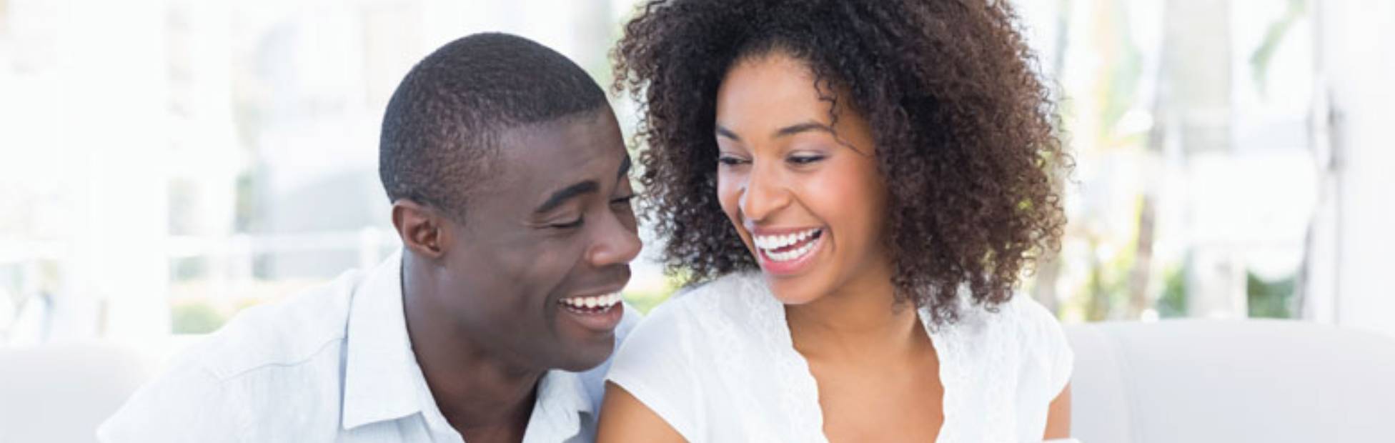 Image d'un couple assis sur un sofa, qui regarde en riant l'écran du téléphone que tient la femme.