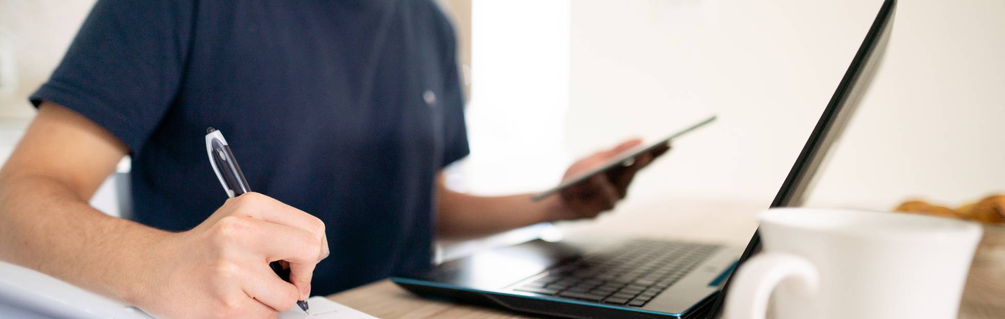 Gros plan d'un jeune homme qui prend des notes en consultant son ordinateur portatif