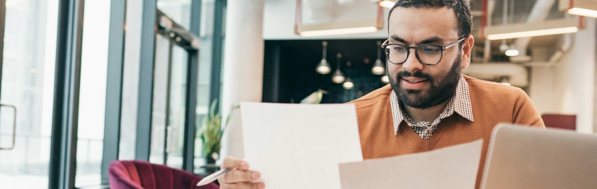Homme examinant des papiers devant un ordinateur portable