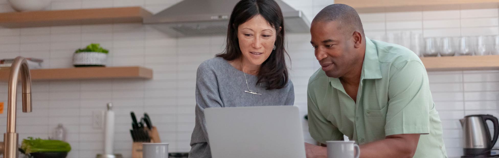 Image d'un couple heureux d'un certain âge qui regarde l'écran d'un portable placé sur le comptoir de cuisine.