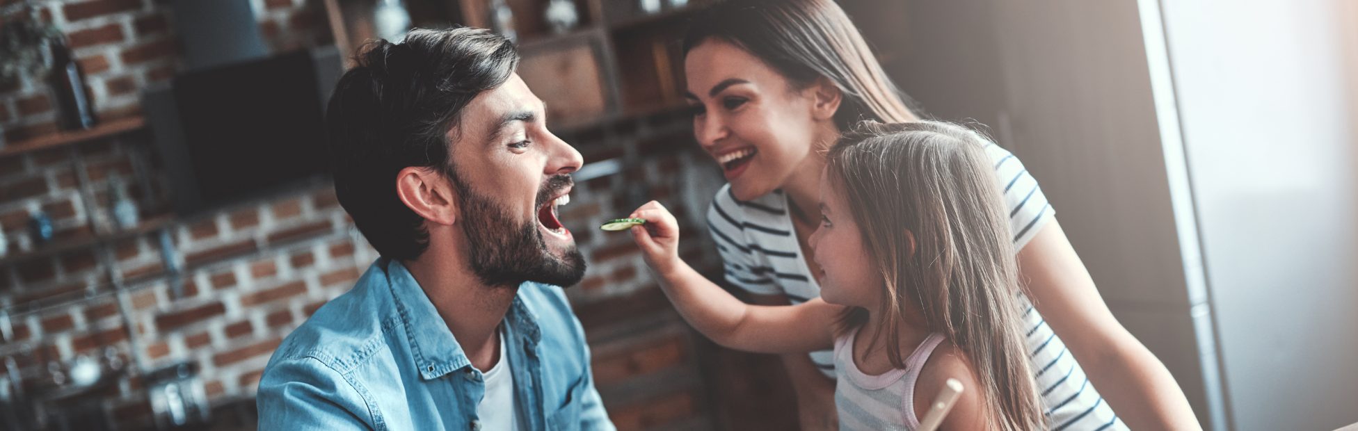 Un père, une mère et leur fille préparent ensemble un repas dans la cuisine.