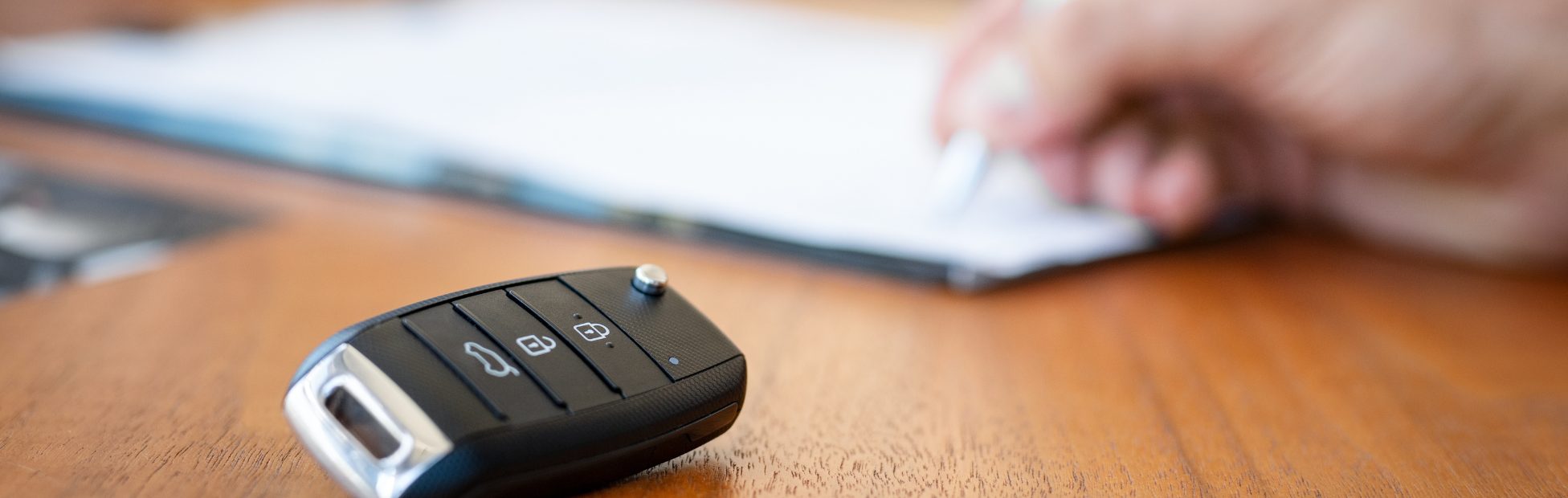 Image d'une main en train de signer un contrat, avec une clé en avant-plan