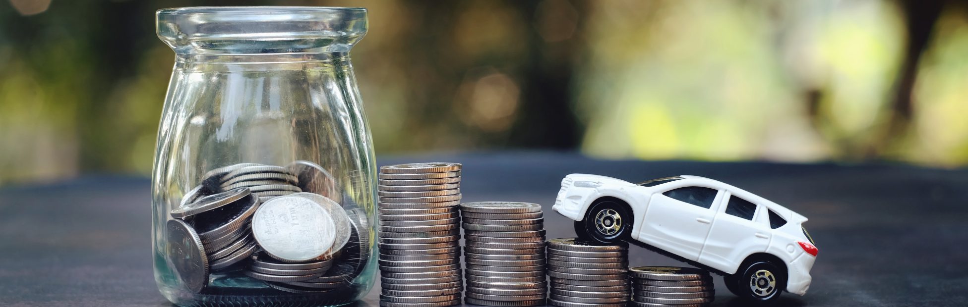 Rangée de piles de pièces de monnaie sur une table et voiture jouet gravissant ces piles
