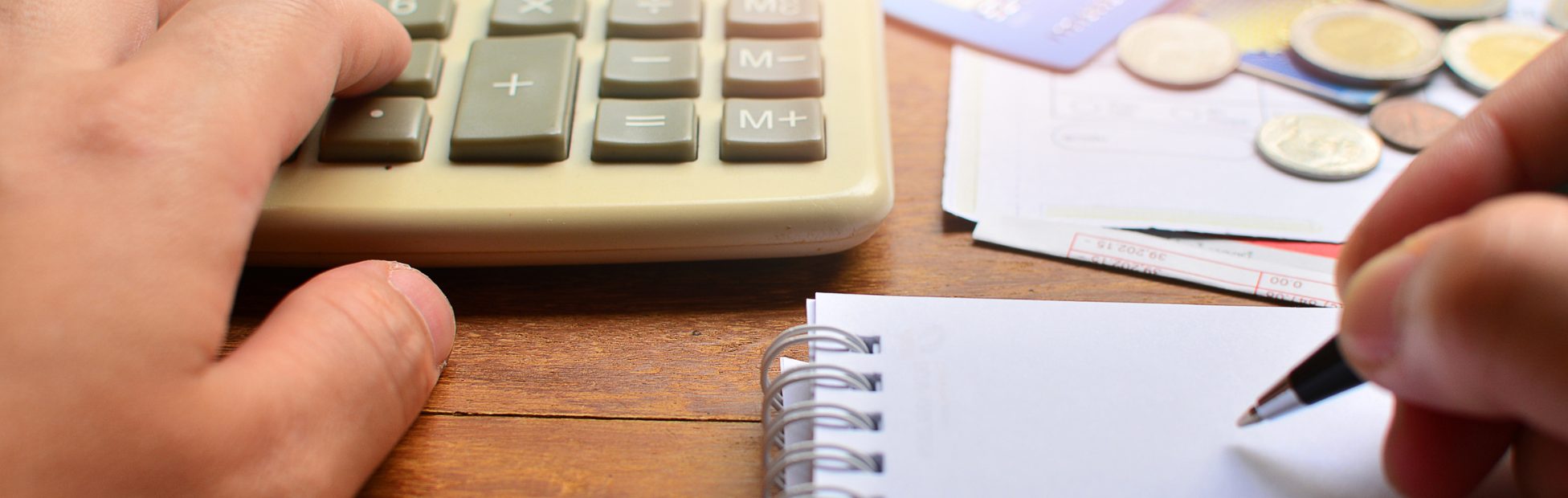Une main posée sur une calculatrice, sur fond flou de cartes de crédit et de pièces de monnaie