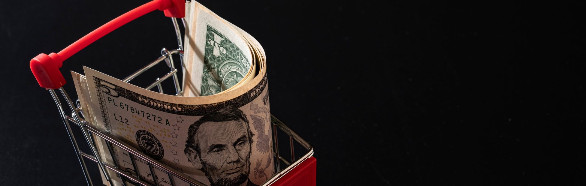 Panier d'achat miniature rempli de dollars américains, sur fond noir
