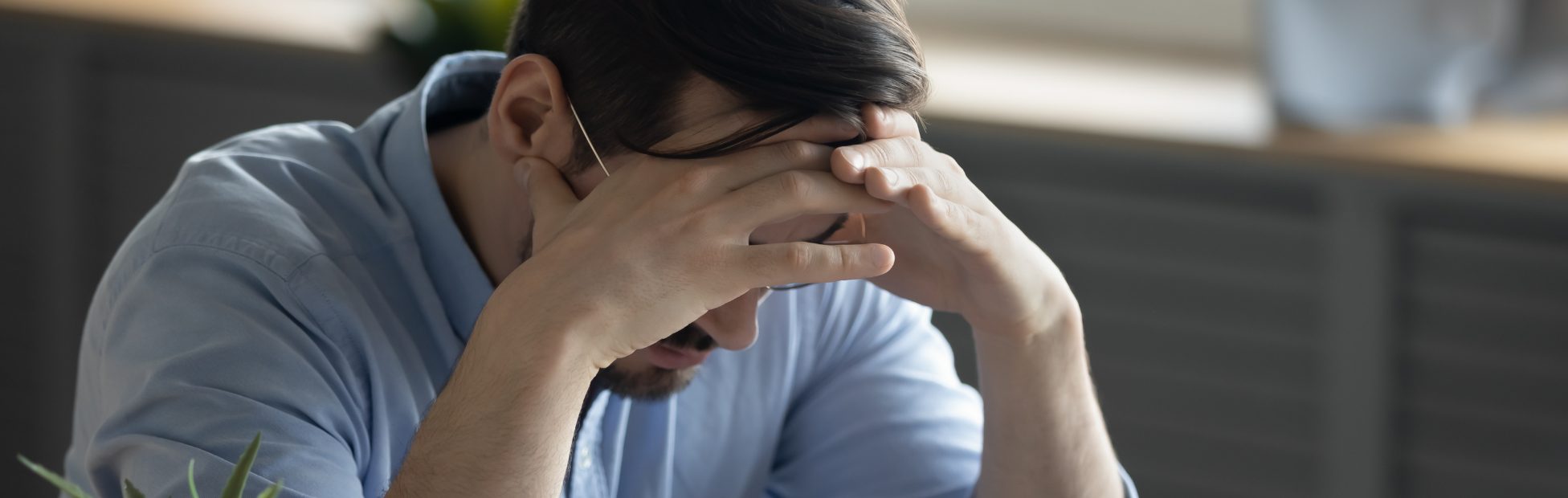 Jeune homme soucieux, assis à son bureau, en train de jongler avec des factures