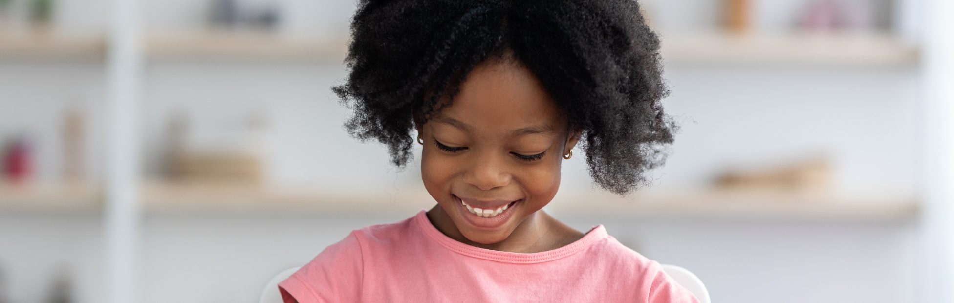 Fillette afro-américaine, souriante, vêtue d'un tee-shirt rose, jouant avec des cubes de bois colorés.
