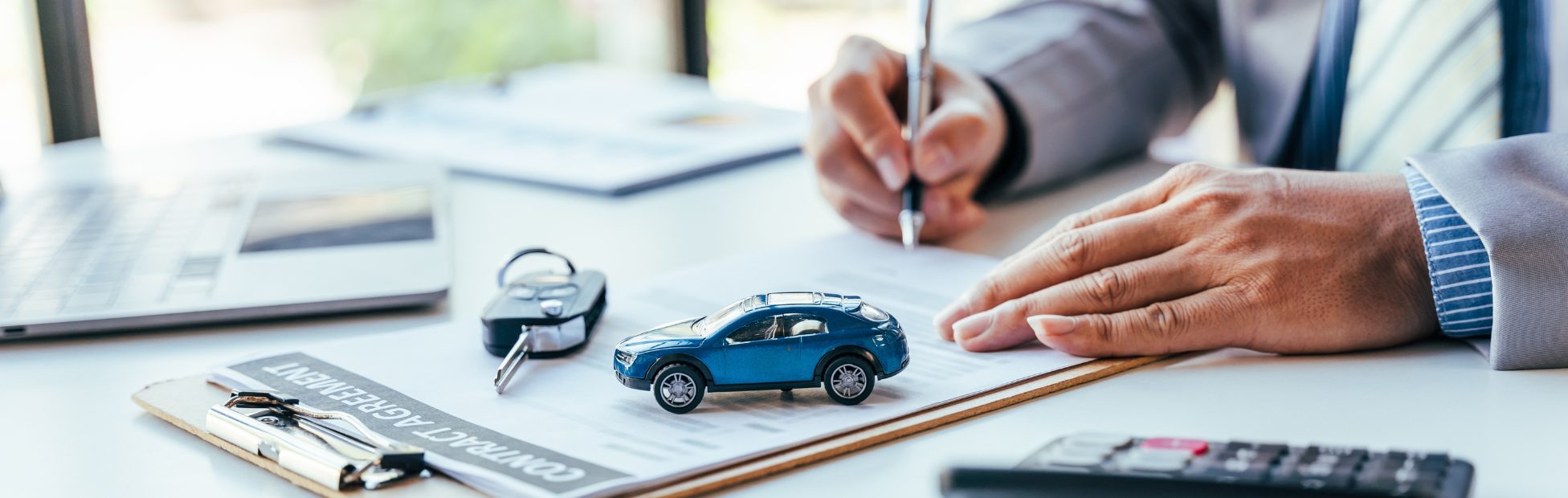 Homme signant une convention de prêt-auto sur un bureau avec une calculatrice à portée de main