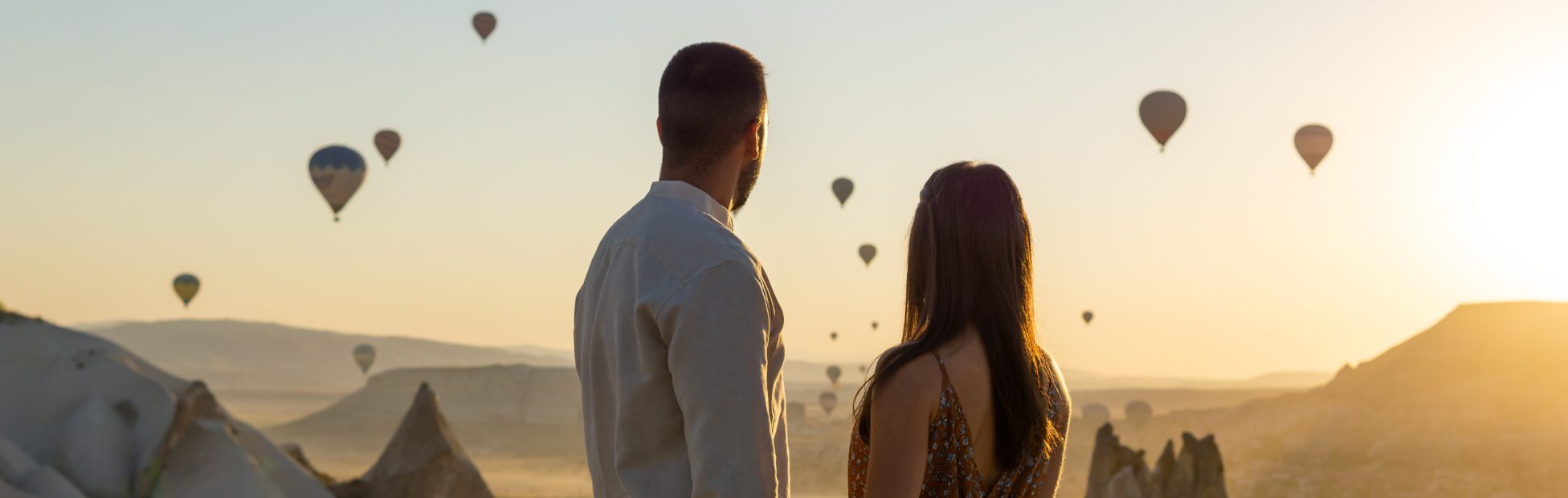 Jeune couple se tenant la main et regardant le soleil se coucher sur les montagnes