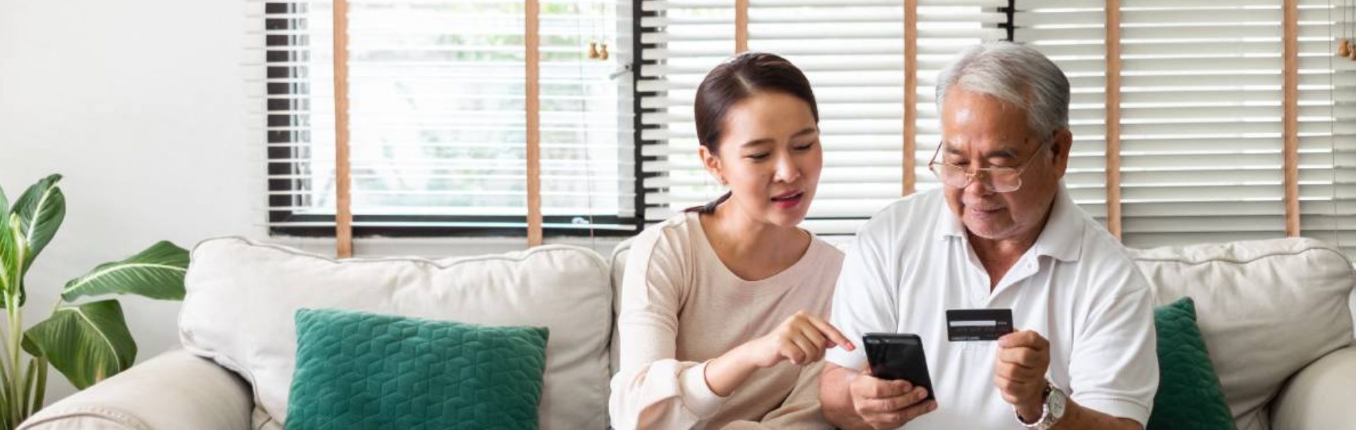 Une femme asiatique explique à un homme plus âgé comment utiliser une carte de crédit et un téléphone pour faire des achats en ligne.