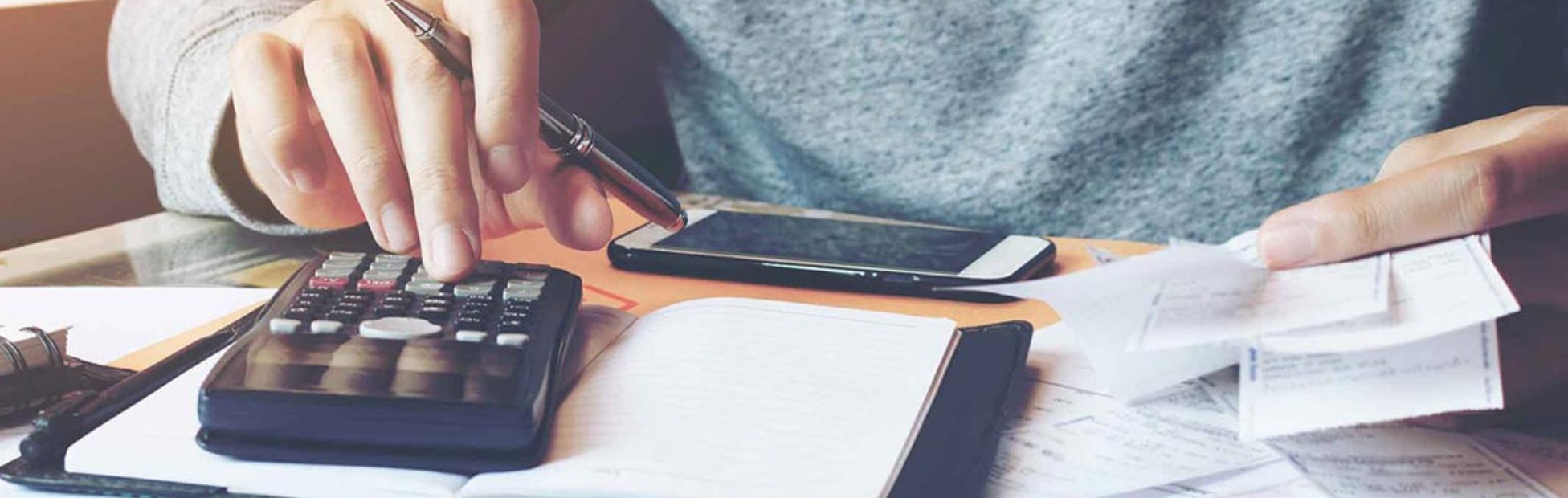 Un homme utilise une calculatrice avec un tas de papiers sur le bureau.