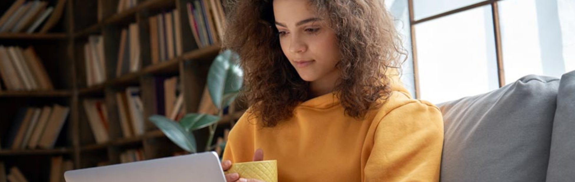Une femme assise sur un canapé regarde son ordinateur portable.