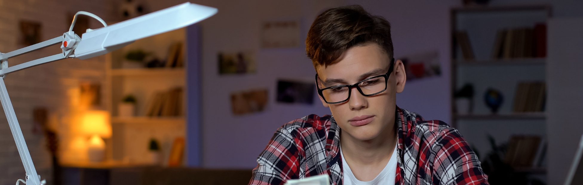 Un adolescent à son bureau compte des billets de banque et les met dans sa tirelire