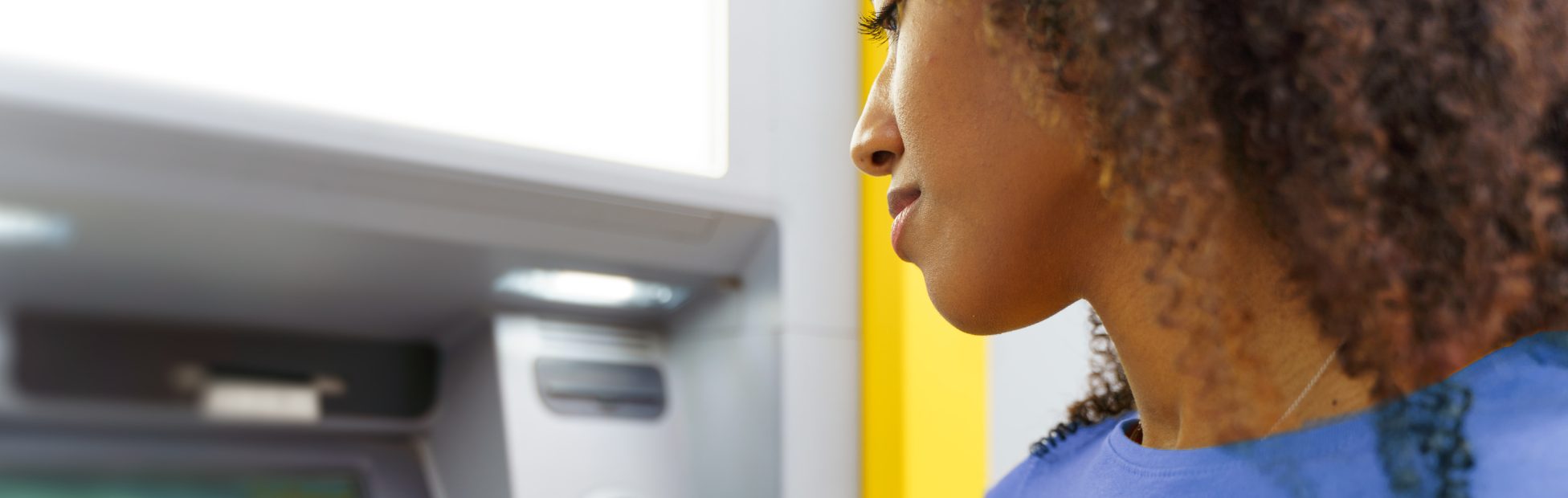 Une jeune femme noire effectue des opérations bancaires au guichet automatique.
