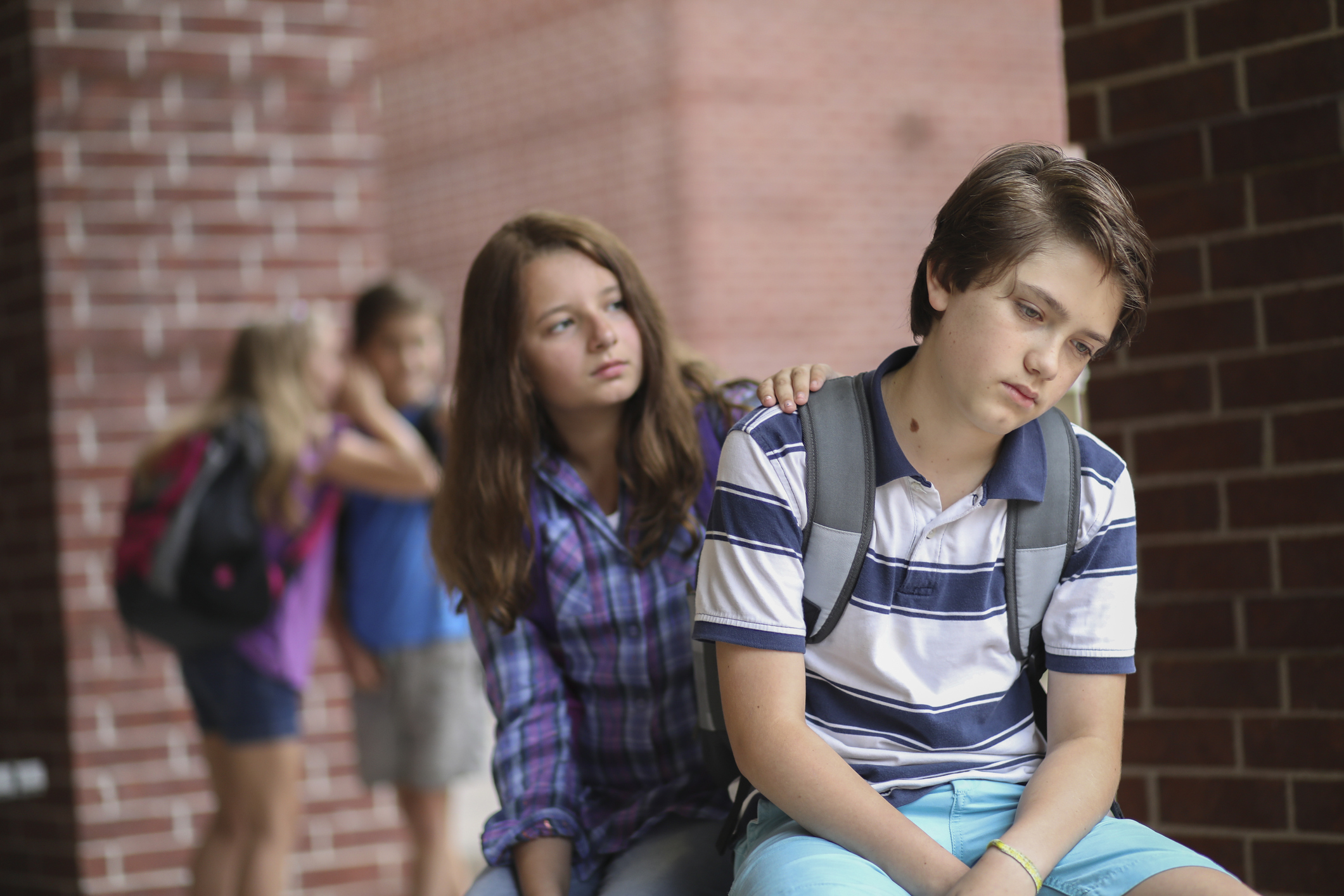 Jeune adolescent triste ou déprimé, réconforté par une amie, avec deux jeunes discutant en arrière-plan.