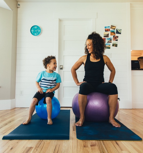 Une mère s'exerce sur un ballon de fitness avec son jeune fils à l'intérieur de leur maison. Elle enseigne au garçon l'importance d'un mode de vie sain en s'étirant et en faisant de l'exercice.
