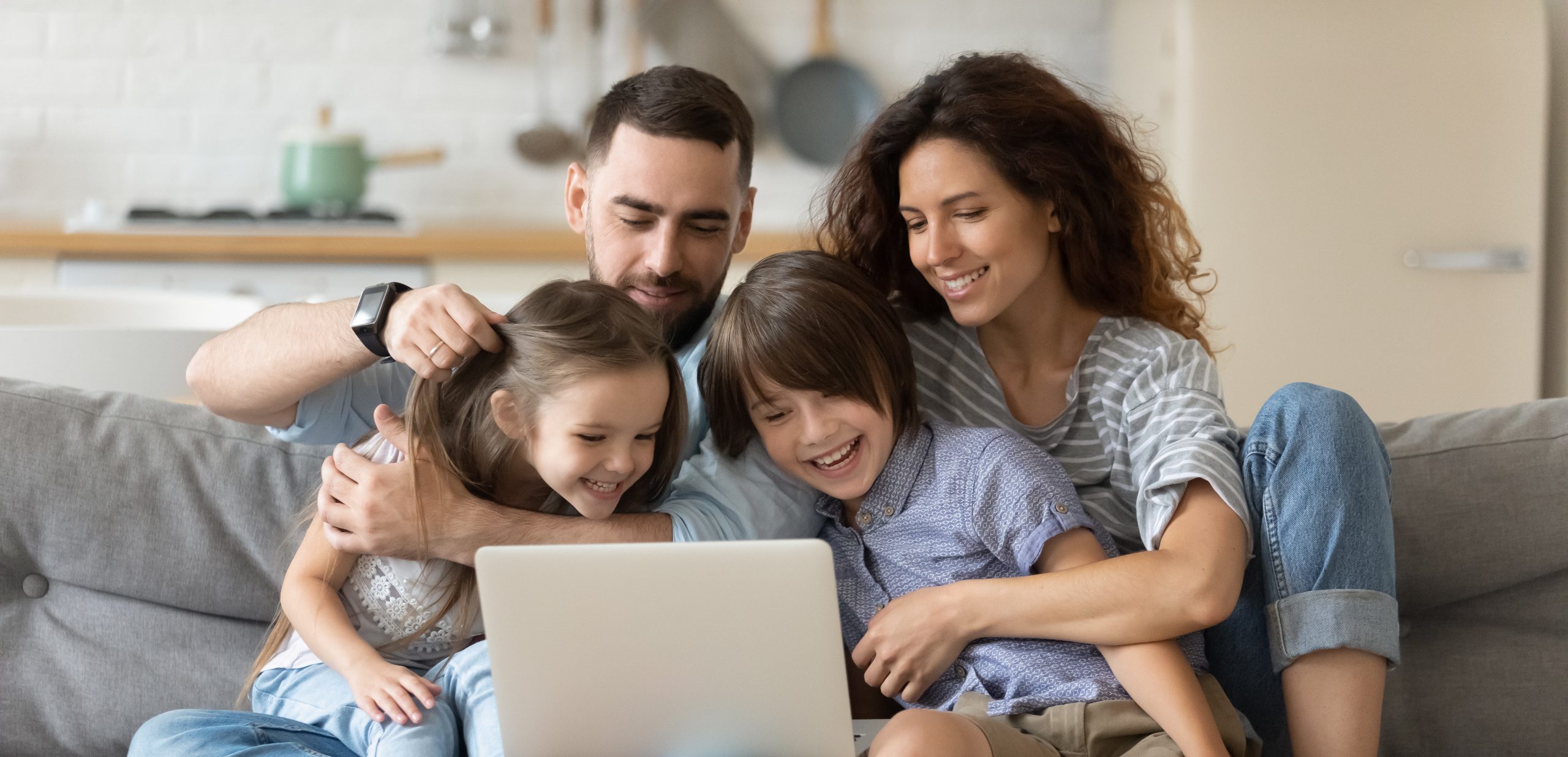 Une jeune famille souriante de quatre personnes assise sur un canapé, regardant un ordinateur portable